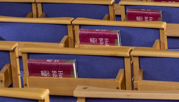 Rows of wooden church chairs with Bibles