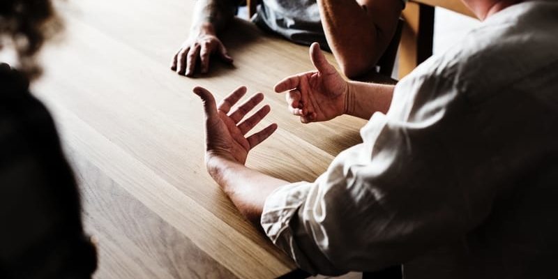 A church event planning committee sits around a wooden table discussing the next event