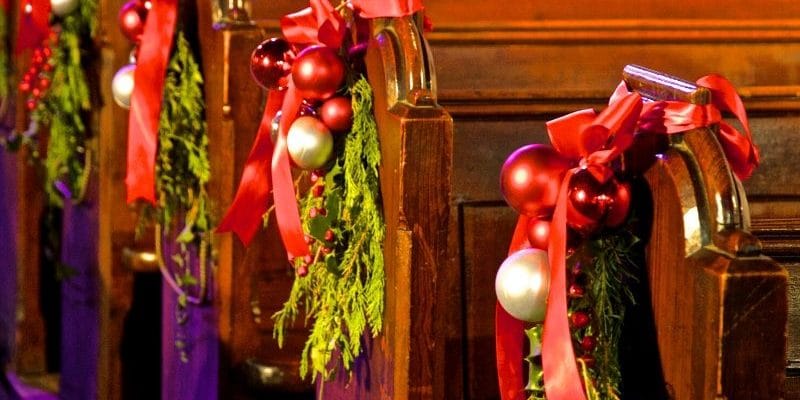 Church pews decorated with Christmas evergreens and red bows