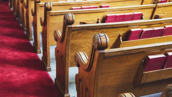 Wooden church pews on tile floor with red carpeting on the center aisle