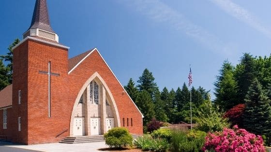 A brick church surrounded by bushes and trees